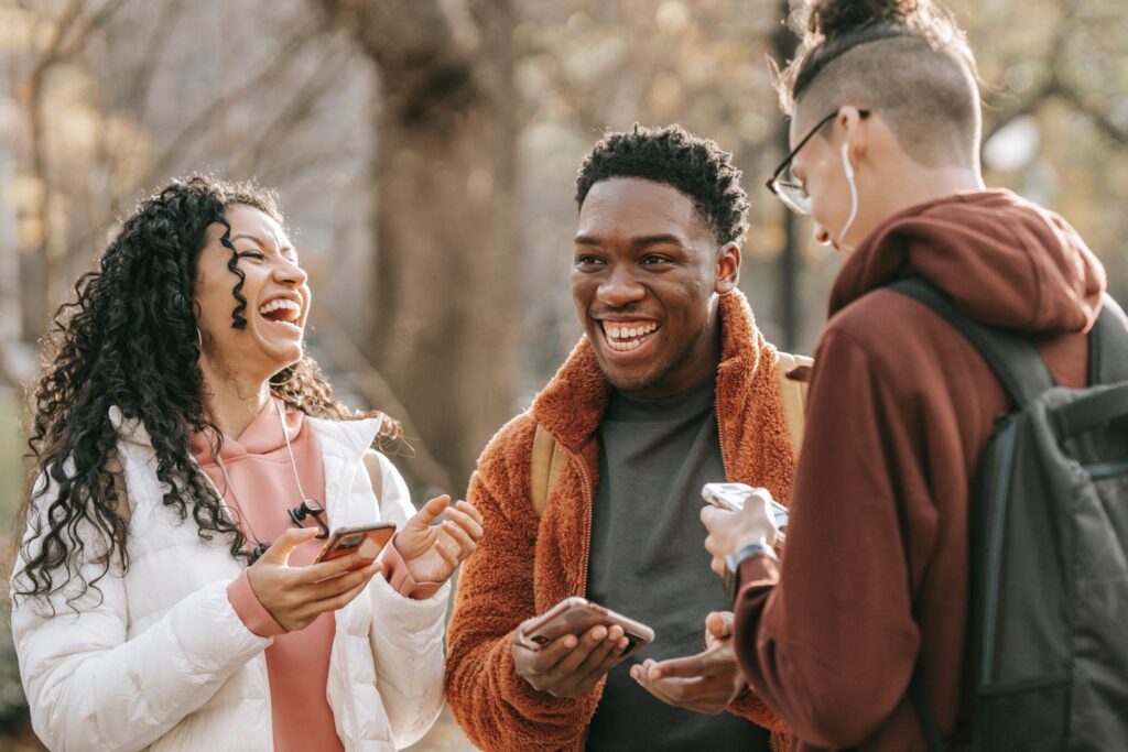 Three people outdoors, two holding smartphones while talking together.