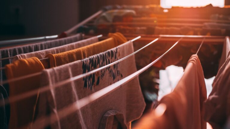 Clothes and towels hanging on an indoor drying rack in warm window light.