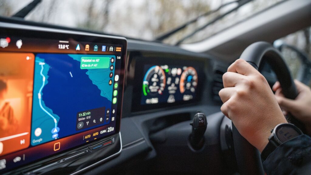 A navigation map on a car dashboard beside hands holding the steering wheel
