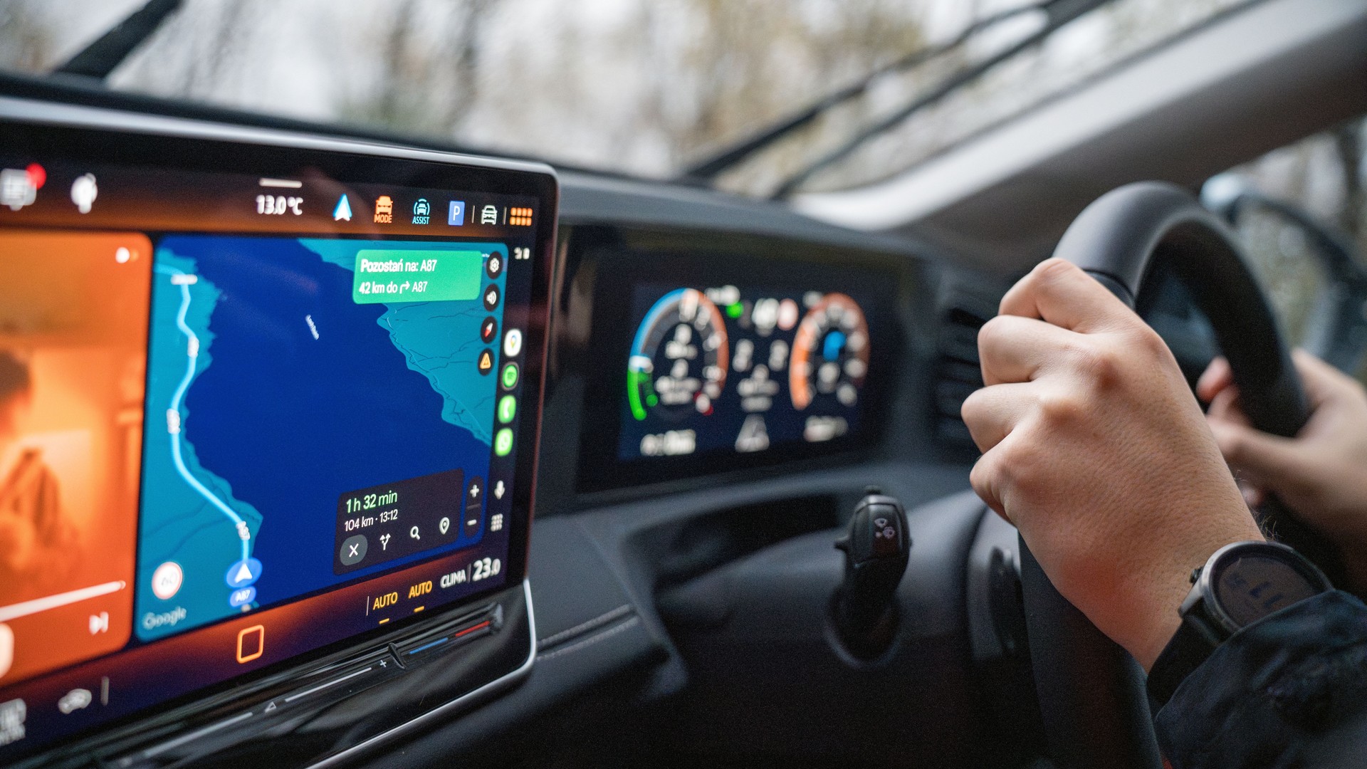 A navigation map on a car dashboard beside hands holding the steering wheel