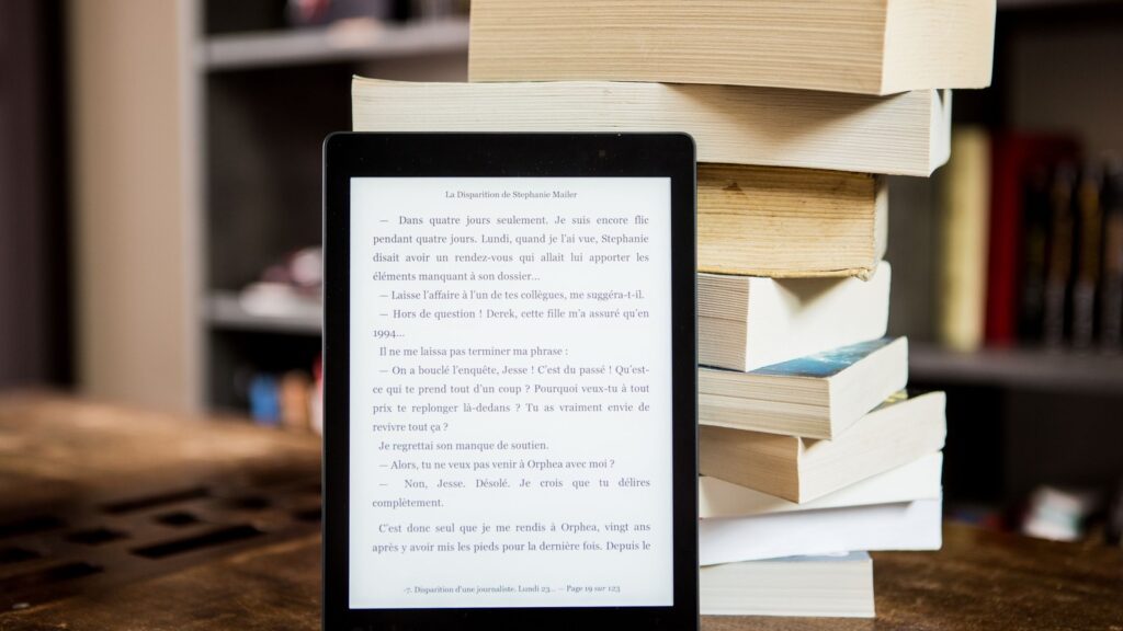 Black e-reader displaying text beside a stack of printed books
