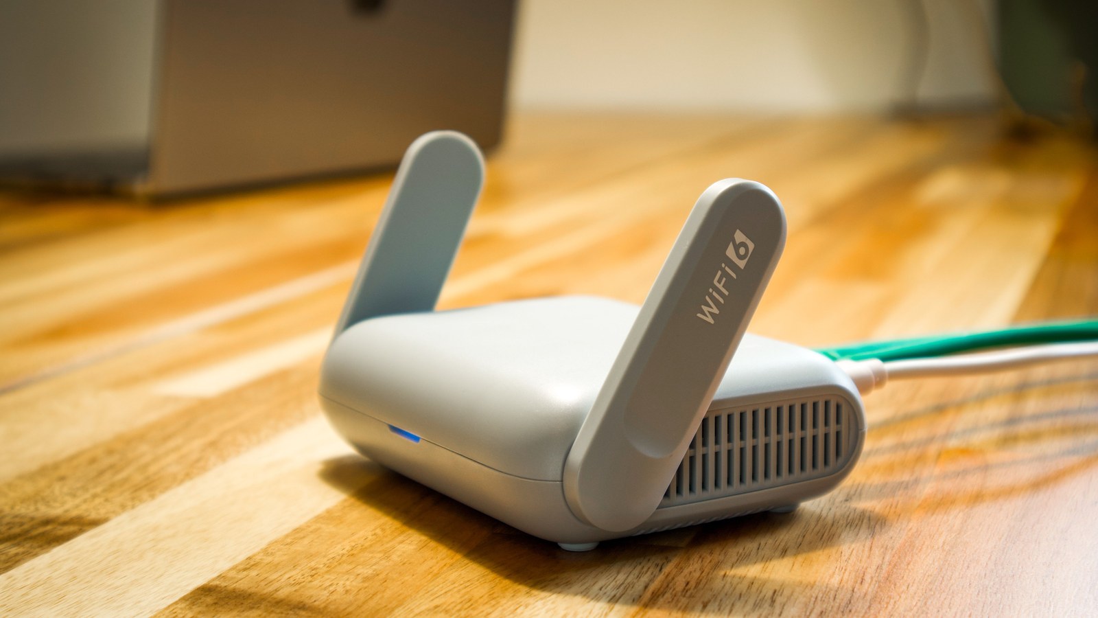 A white Wi-Fi router with two antennas and connected cables on a wooden desk.