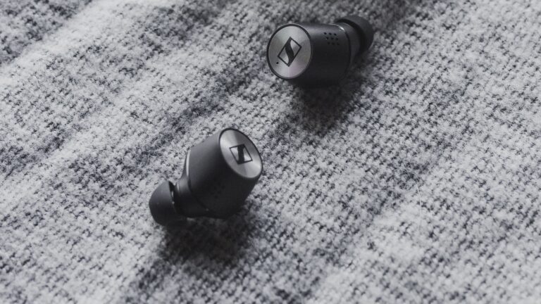 Two black wireless earbuds on textured grey fabric