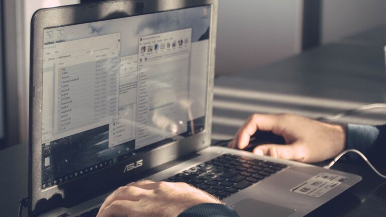 Hands using an ASUS laptop with Windows file windows on the screen.
